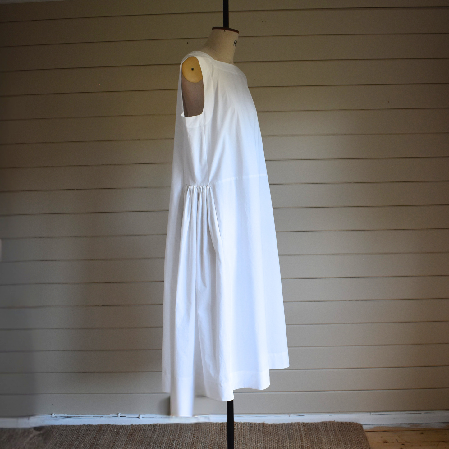 White dress on a mannequin against a wooden paneled wall.